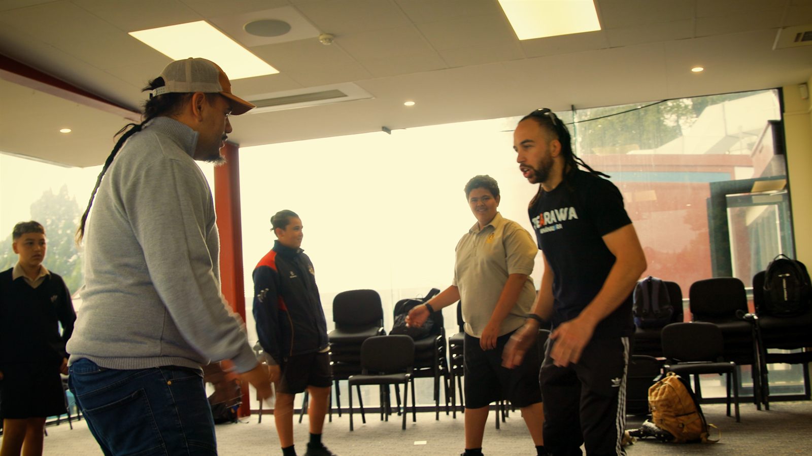 Kaimahi and rangatahi standing together in a school hall during a session